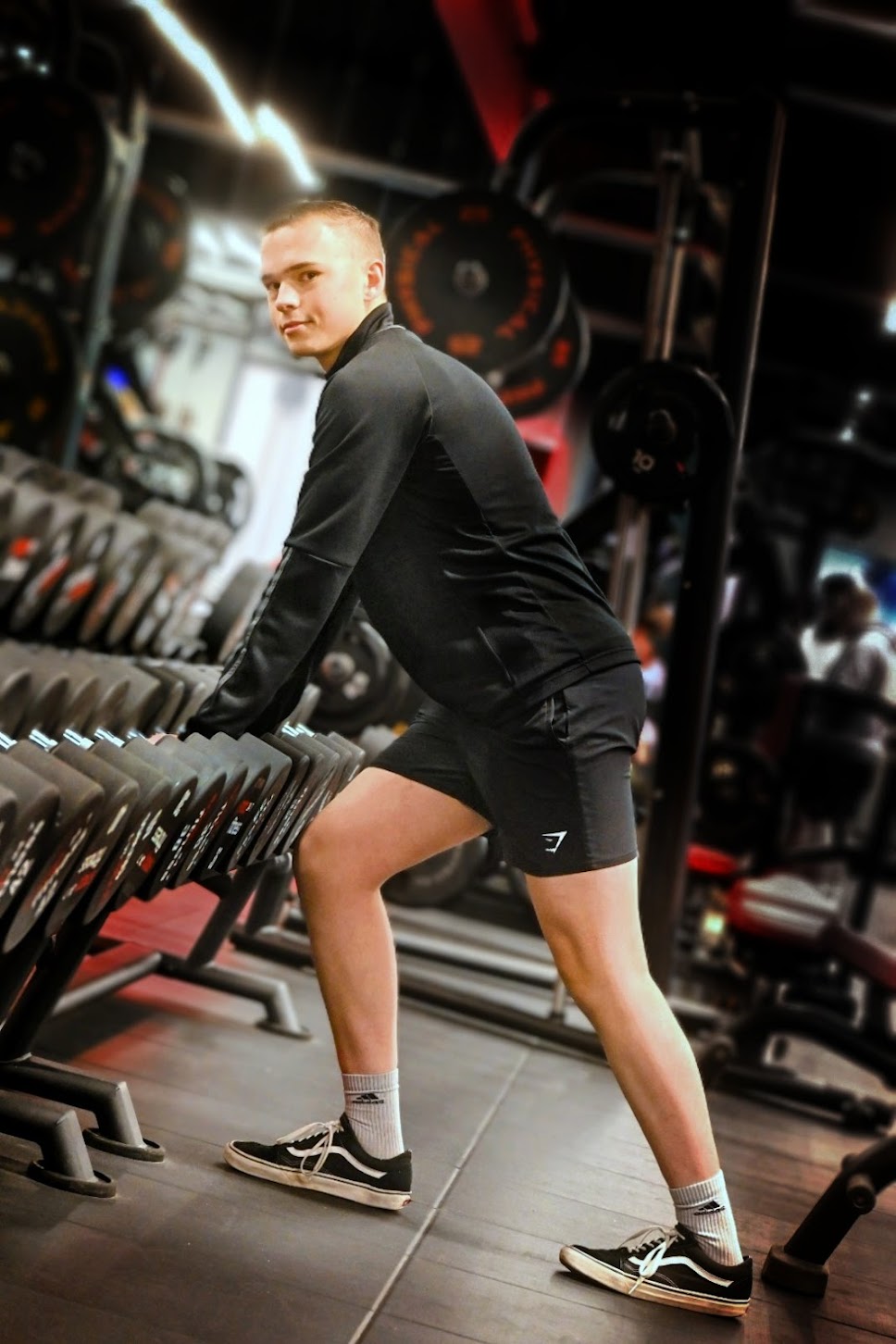 Joe Penrose about to pick up some weights from the dumbbell rack, while looking at the camera.